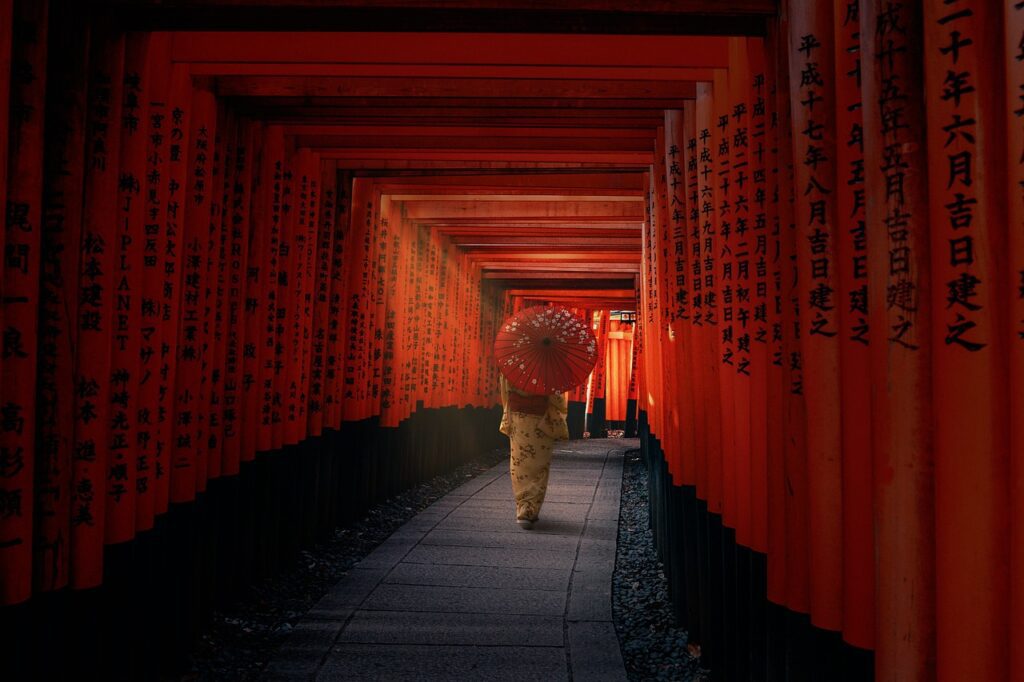 A person in traditional Japanese dress walking down a red corridor holding a Japanese umbrella