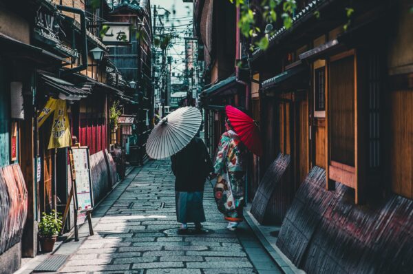 Two people walking down a street holding Japanese umbrellas