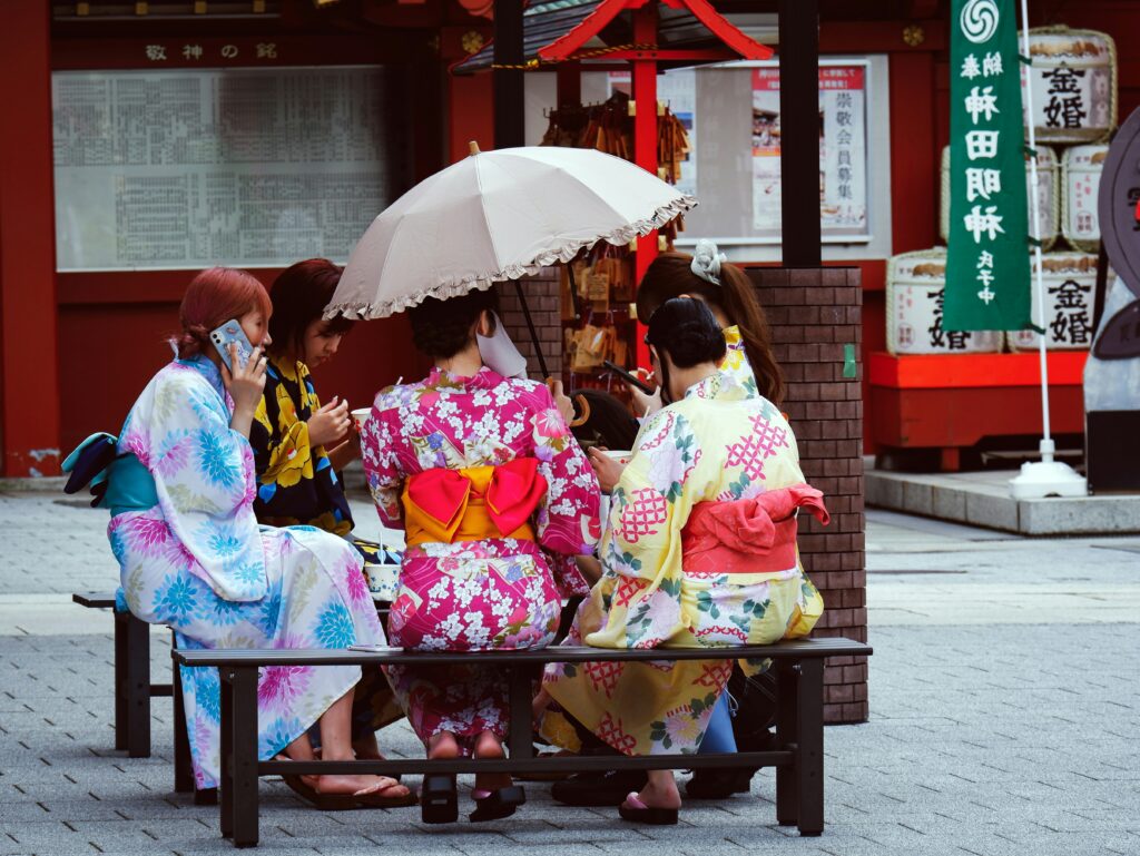 A group of Japanese women sat under an umbrella on a bench in colourful Japanese attire