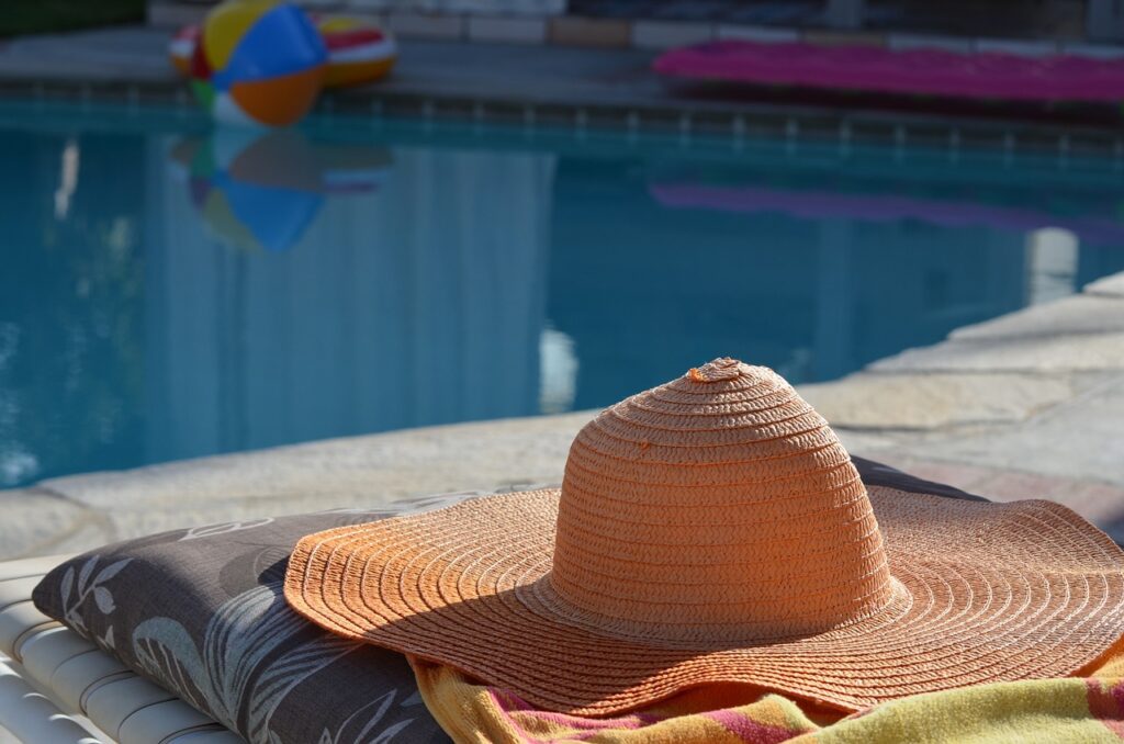 A wide brimmed hat on a towel next to a pool
