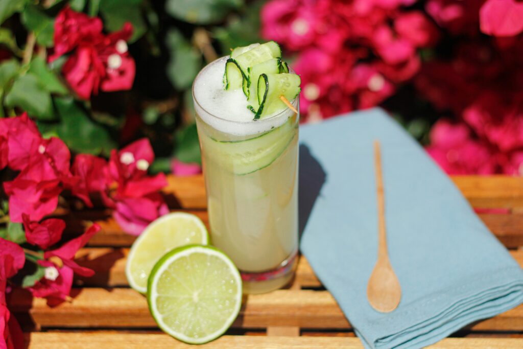 A cucumber and lime drink on a bench surrounded by pink flowers