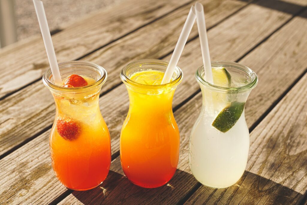 Three glass pitchers of fruit juices with straws taken outside on wooden decking