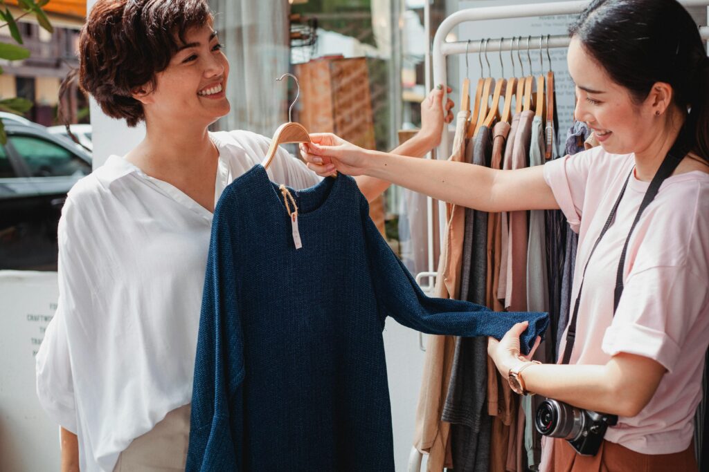 Two women are holding up a jumper at a clothes store.