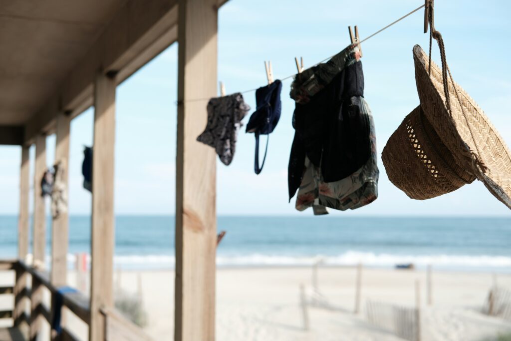 Various items of clothing such as a hat, shorts and bikni are hanging on a washing line at the beach.