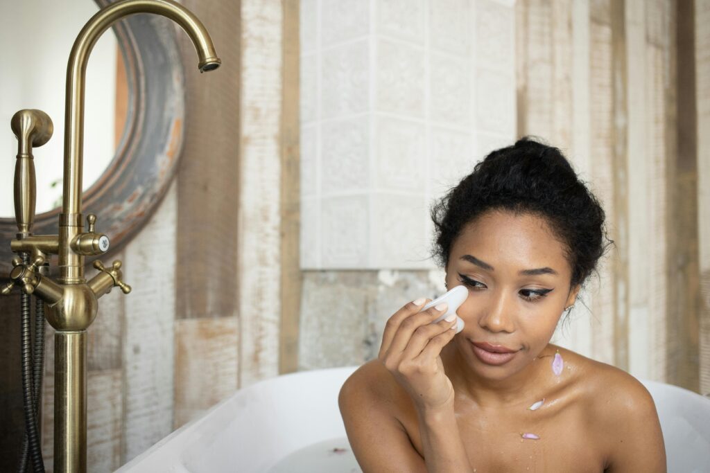 A woman in a bath using a gua sha tool on her face