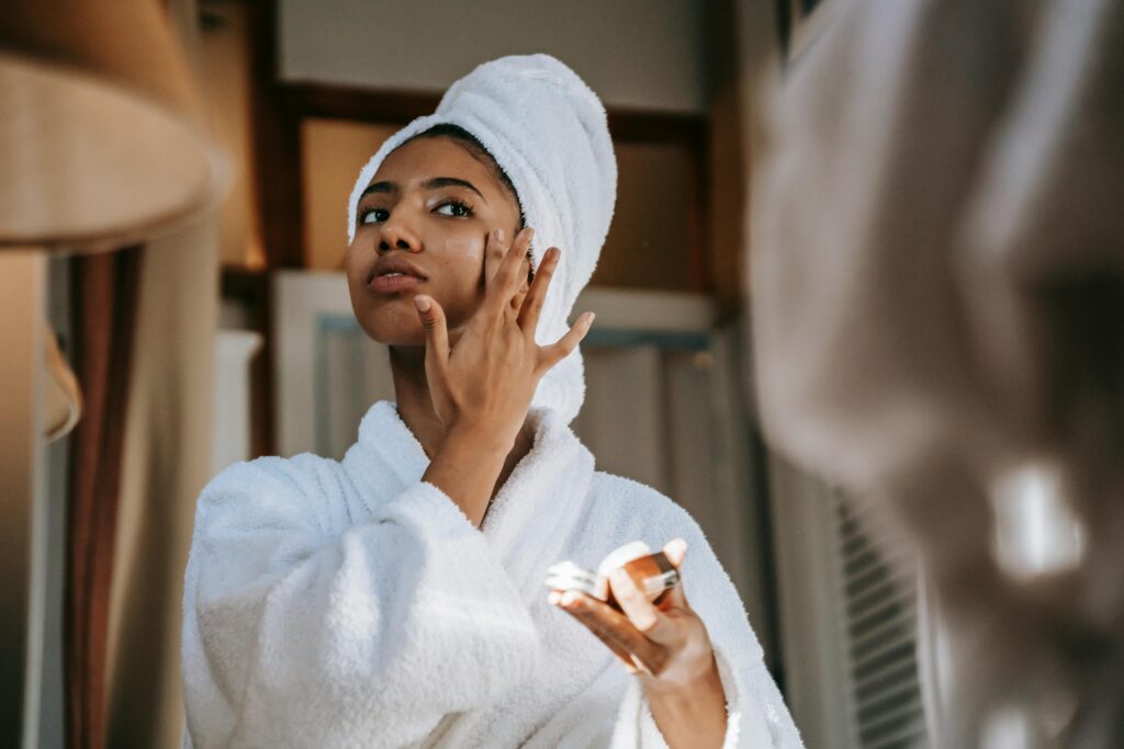 A woman in a robe and towel turban applying moisturiser to her face