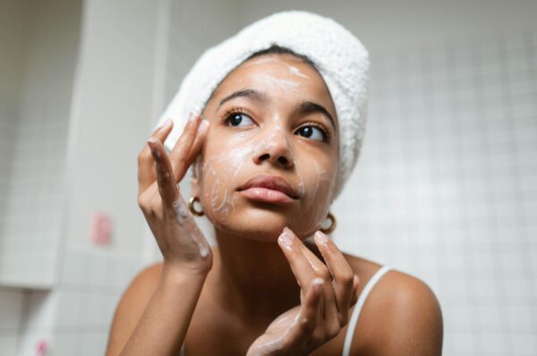 A woman with her hair wrapped in a towel leans in to apply a product to her face